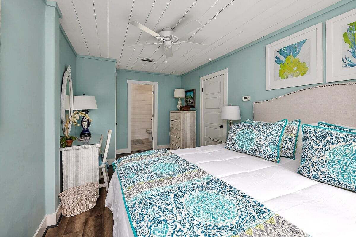 Ein Schlafzimmer mit Bett, Deckenventilator, Kommode, Spiegel, Lampe und Bildern an der Wand.