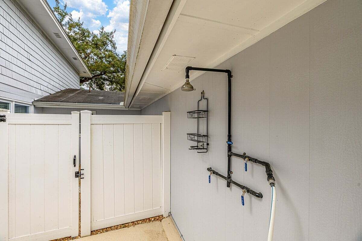 Eine weiße Außenwand mit einem Wasserhahn aus Metall, einem Metallregal und einer Deckenleuchte.