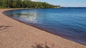 Une plage à l’eau claire, un rivage sablonneux et une zone boisée en arrière-plan.