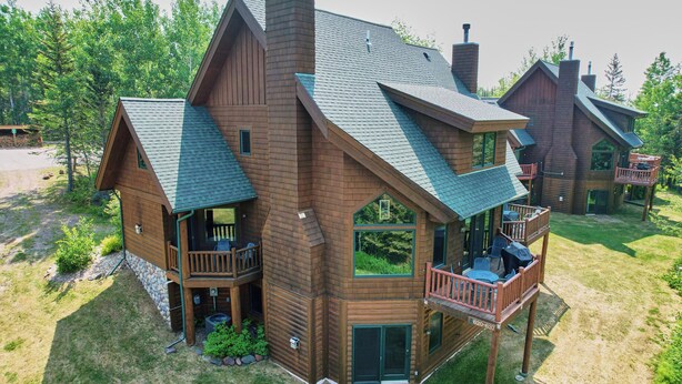 Une grande cabane en rondins à plusieurs étages, dotée d’une véranda qui fait le tour de la maison et d’une terrasse.
