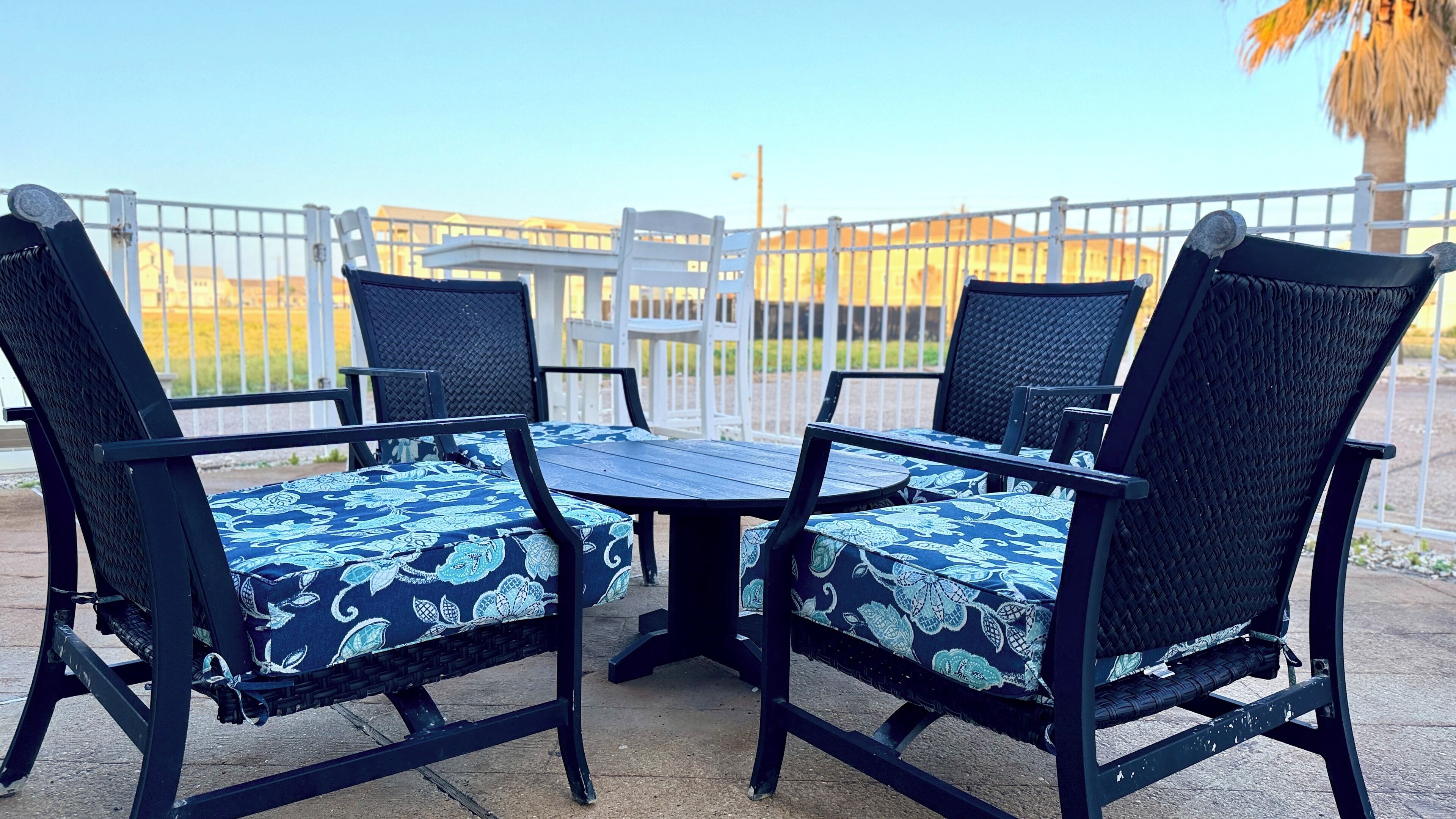 An outdoor patio with a table and four chairs, surrounded by a white fence.