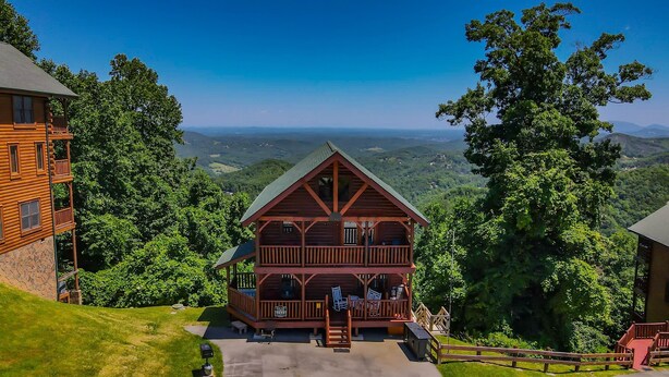 A log cabin with a balcony, surrounded by lush greenery and a scenic view of the mountains.