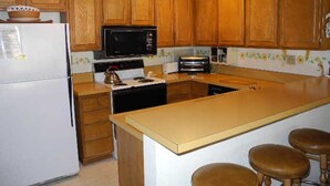 A kitchen with wooden cabinets, a microwave, a stove, and a sink. There are stools at the island. - Courchevel 56 (Mammoth Lakes)