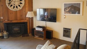 A living room with a fireplace, a mounted clock, a television, and a framed picture on the wall. - Courchevel 56 (Mammoth Lakes)