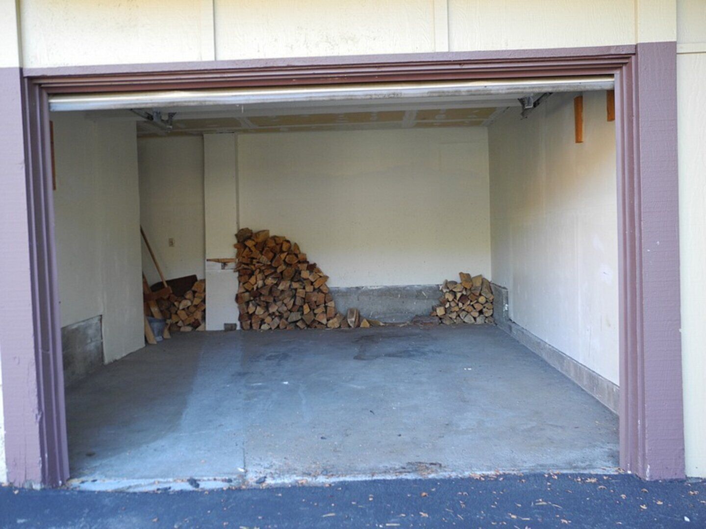 A garage with a concrete floor and a stack of firewood against the wall.