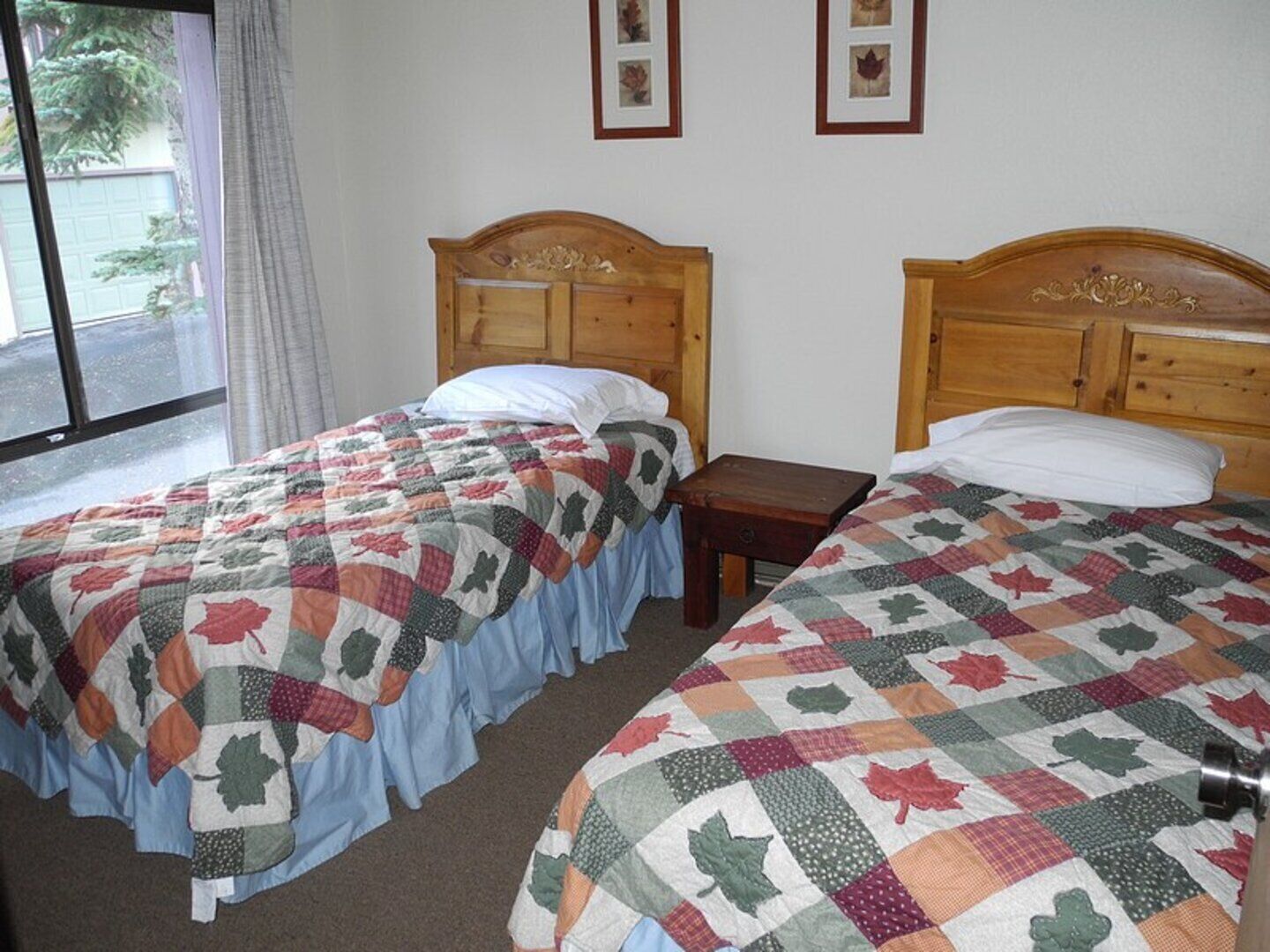 Two single beds with matching headboards, a wooden nightstand, and a window with a view of a street and trees.