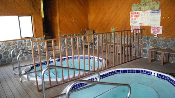 A pool area with two hot tubs, wooden walls, and a stone wall in the background. - Courchevel 56 (Mammoth Lakes)