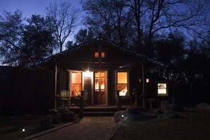 Une cabane avec une véranda, une cheminée et des guirlandes lumineuses.