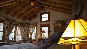 Une chambre confortable avec des poutres en bois, un lit recouvert d’une literie à motifs floraux, un bureau et une fenêtre avec des rideaux.