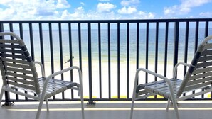 Dos sillas de metal blanco en un balcón con vistas al océano y la playa.