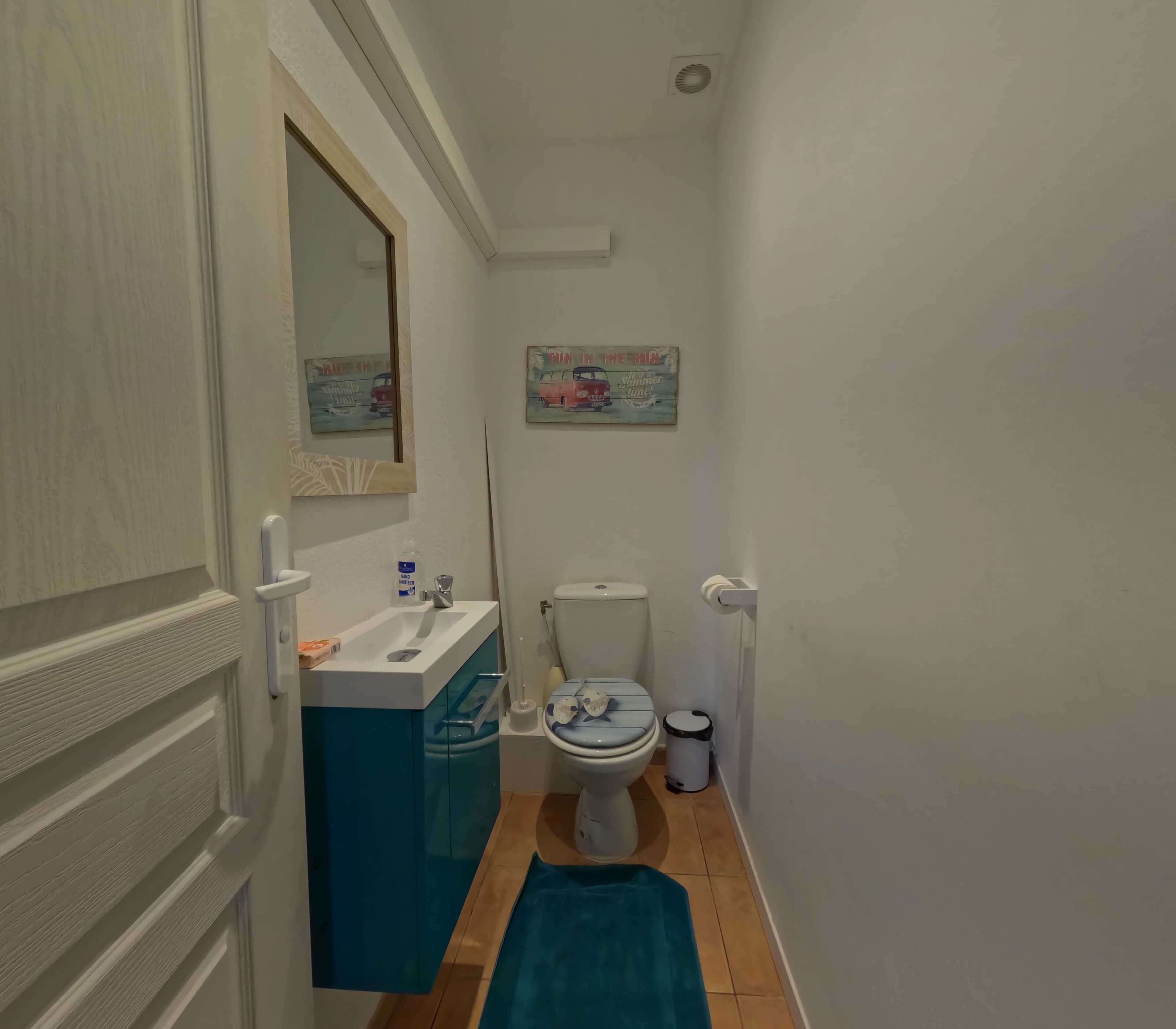 Een kleine badkamer met een wit wastafelblad, een blauwe kast, toilet en een blauw vloerkleed.