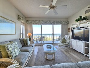 A living room with a sofa, a coffee table, a TV, and a balcony with a view. - Oceanfront Villa w/ Balcony, Views & Amenities (Hilton Head Island)