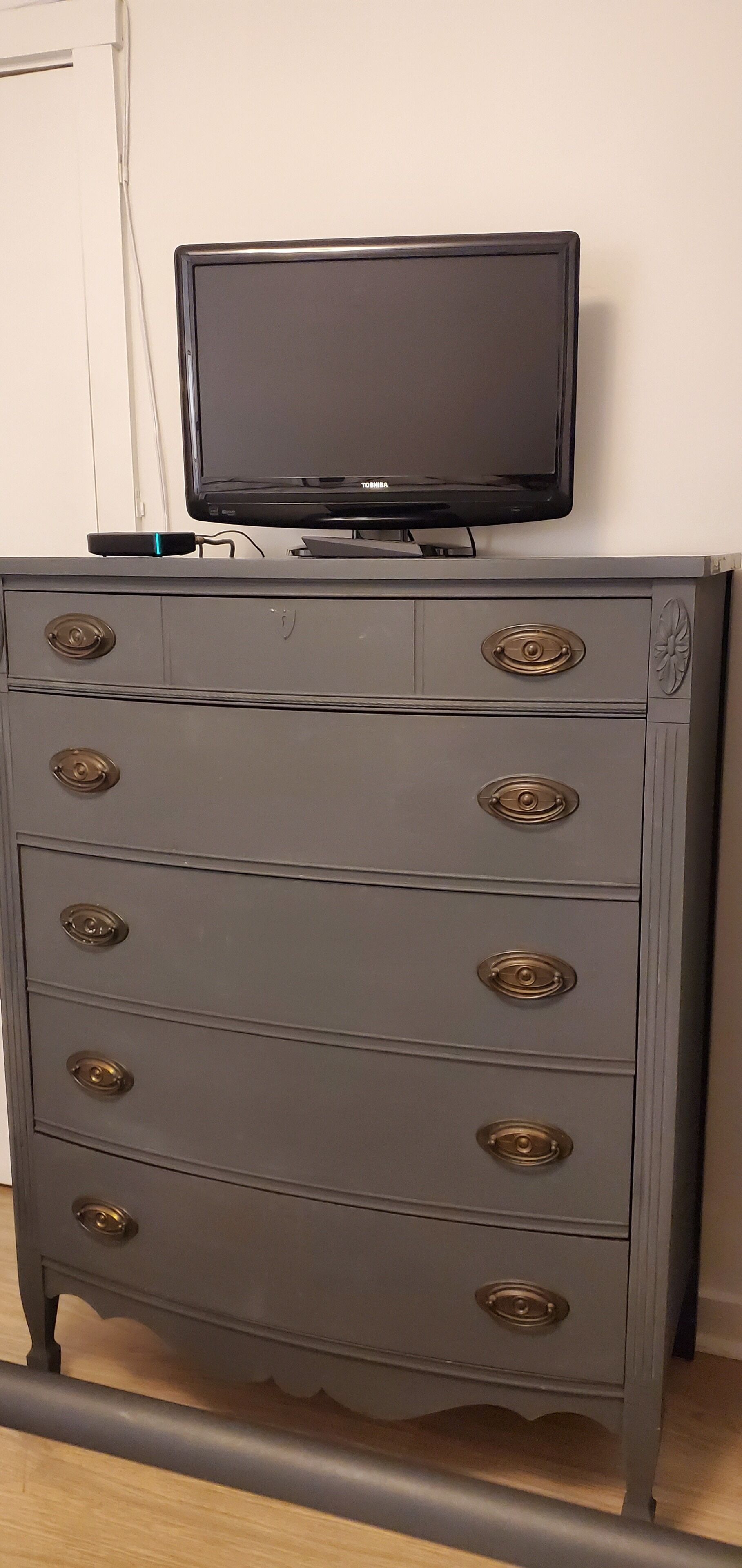 A grey dresser with multiple drawers and a flat-screen TV on top.