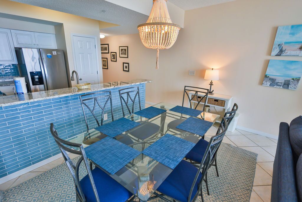 A modern kitchen with a blue tiled backsplash, stainless steel appliances, and a glass dining table with blue placemats.