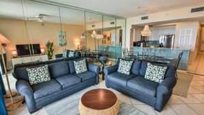 A living room with two sofas, a coffee table, and a dining area with a glass partition. - Majestic Sun 1005A - Great Views, Discount Golf, Discount Beach Service! (Miramar Beach)