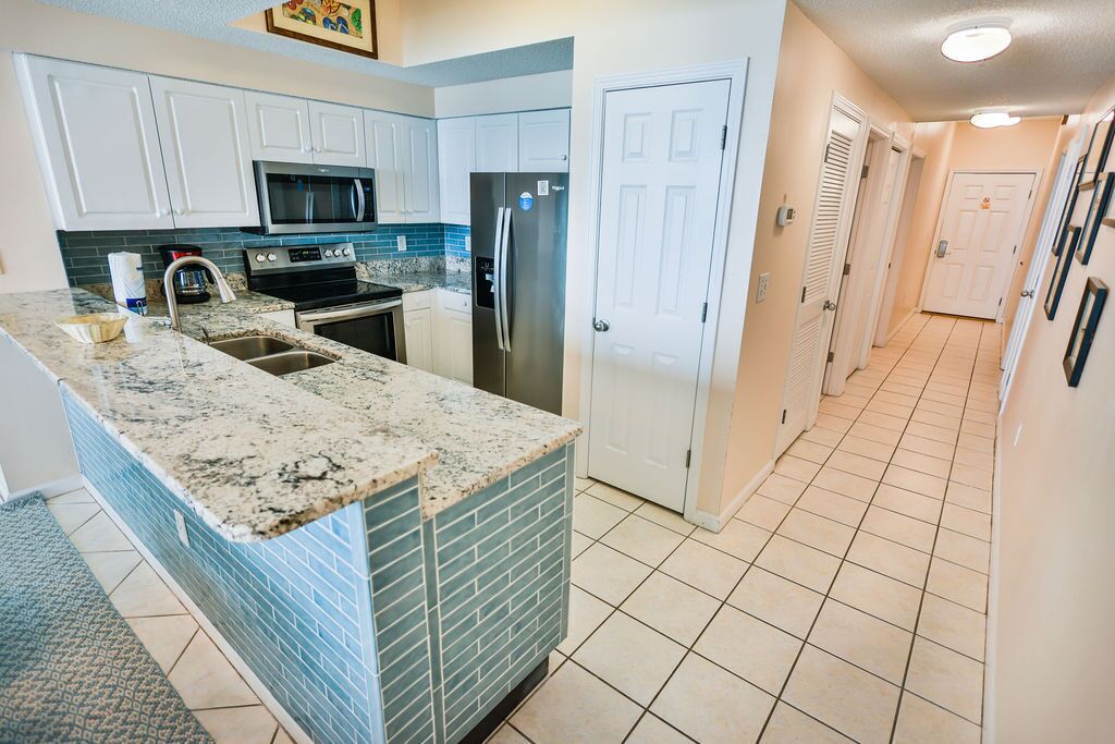 A kitchen with white cabinets, a granite countertop, a stainless steel refrigerator, and a microwave.