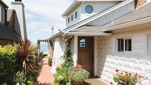 A coastal house with a covered porch, a wooden door, and a brick chimney.