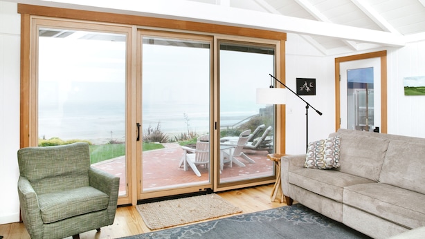 A living room with a sofa, armchair, and a view of the ocean through large sliding glass doors.