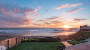A beach view with a sunset, a wooden fence, a grassy area, and a building with a staircase.