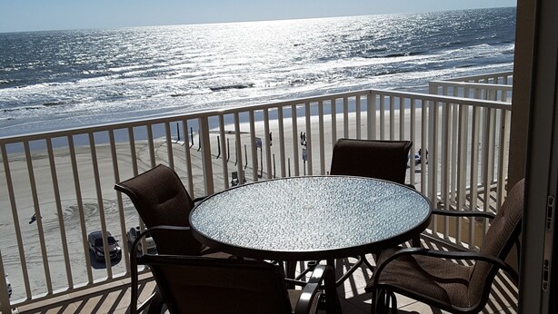 A balcony with a round table and chairs, overlooking the ocean.