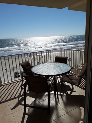 A balcony with a round table and chairs, overlooking the ocean.