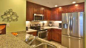 A kitchen with wooden cabinets, stainless steel appliances, granite countertops, and a wall-mounted coffee maker.