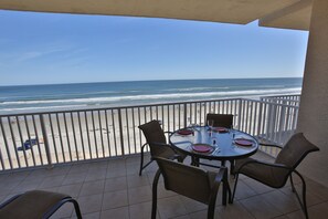 A balcony with a table set for dining, overlooking a beach with a railing.