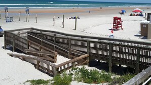 A beach with a wooden boardwalk, beach chairs, umbrellas, and a lifeguard tower.