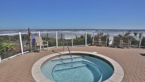A pool with a view of the beach, surrounded by chairs and a fence.