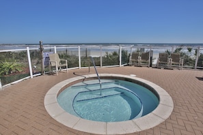 Piscina com vista para a praia, cercada por cadeiras e um gradil.