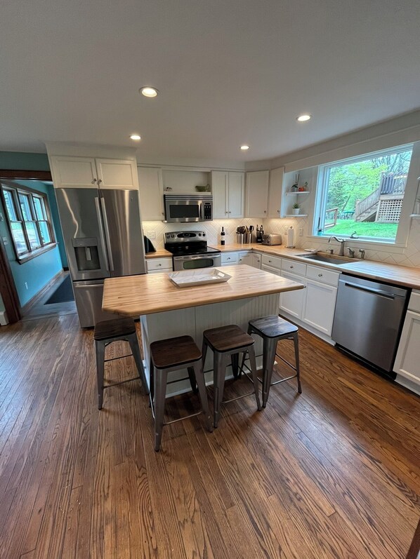 A modern kitchen with white cabinets, stainless steel appliances, and a wooden island with bar stools.