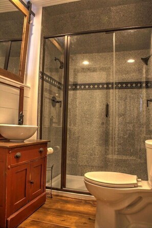 A bathroom with a wooden vanity, a white sink, and a glass-enclosed shower.