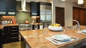 A modern kitchen with dark cabinetry, a stainless steel refrigerator, a gas stove, and a granite countertop.