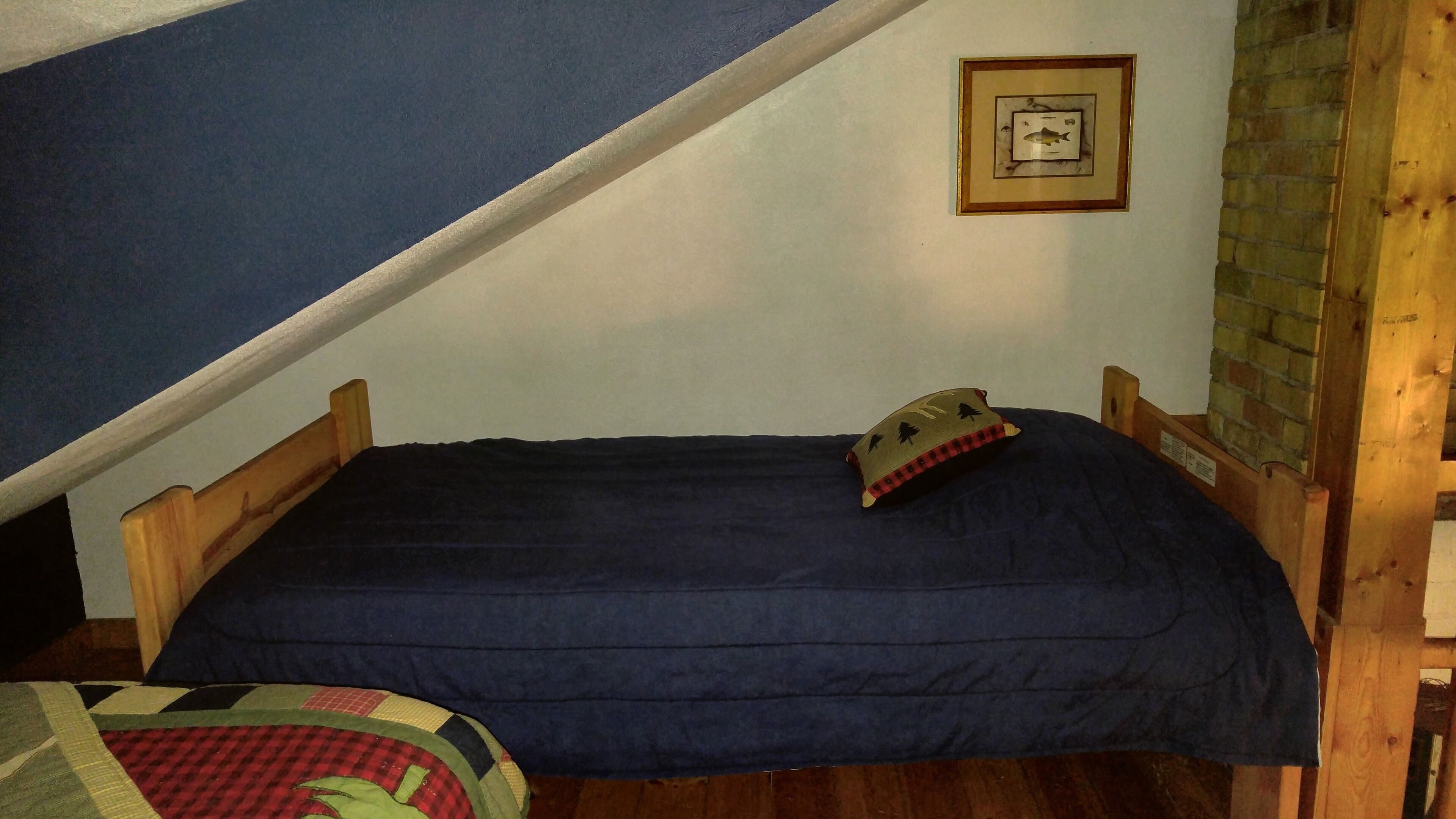 Une petite chambre à coucher, chaleureuse et accueillante, avec un lit simple, une tête de lit en bois, un oreiller et un tableau encadré accroché au mur.