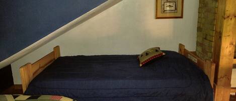 Une petite chambre à coucher, chaleureuse et accueillante, avec un lit simple, une tête de lit en bois, un oreiller et un tableau encadré accroché au mur.