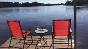 A wooden dock with two red chairs and a small round table with drinks and snacks. - Lakeside cabin retreat; perfect getaway for winter sports, four seasons of fun (Hayward)