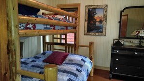 A bunk bed with a plaid bedspread and a red pillow, a wooden dresser, a mirror, and a framed picture of a landscape. - Lakeside cabin retreat; perfect getaway for winter sports, four seasons of fun (Hayward)