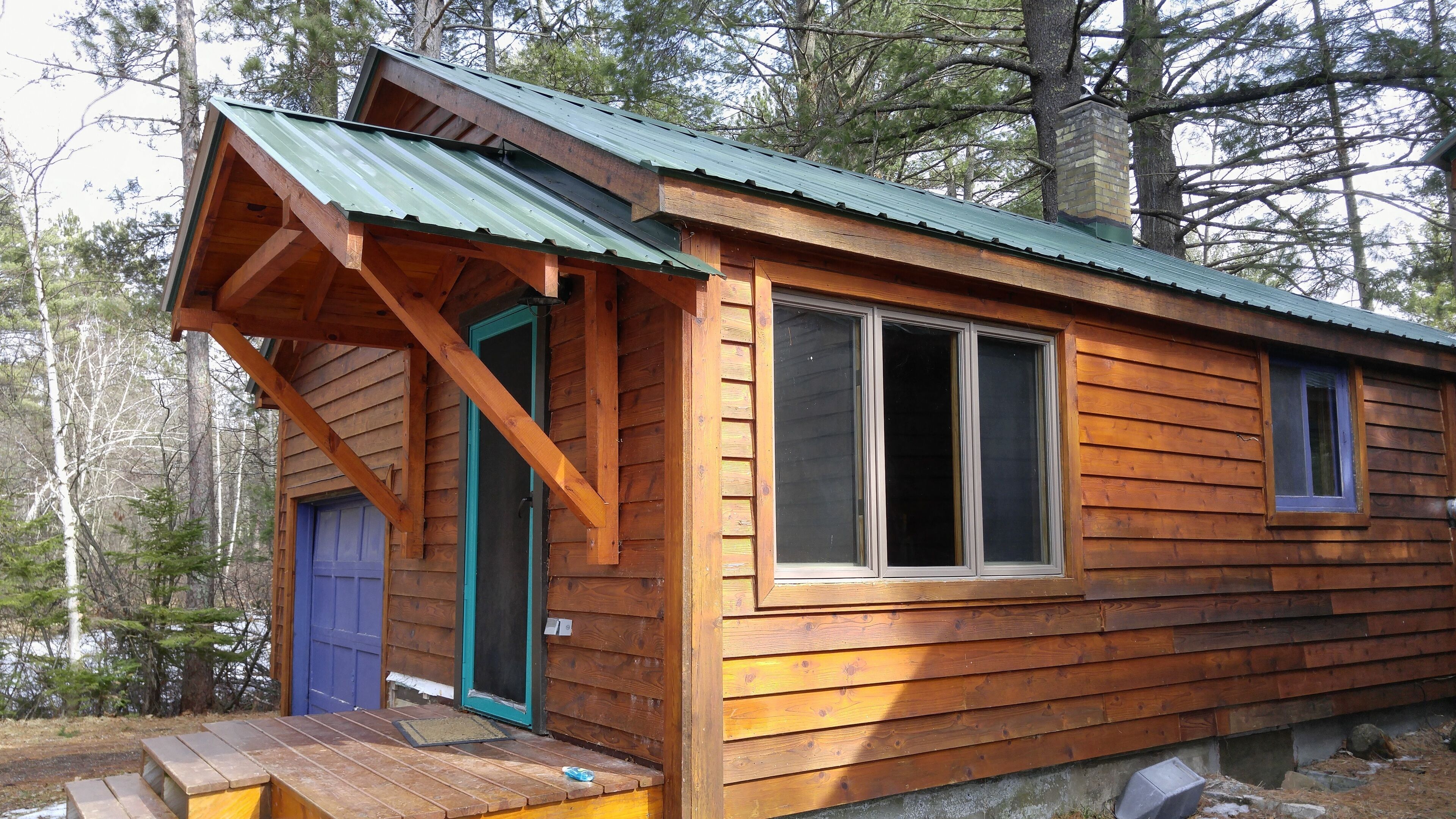 A wooden cabin with a green roof, a blue door, and a small porch.