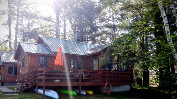 A wooden cabin with a metal roof, surrounded by trees. - Lakeside cabin retreat; perfect getaway for winter sports, four seasons of fun (Hayward)