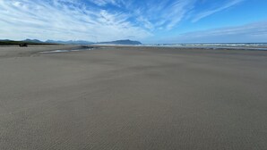 A wide, open beach with a clear sky and distant mountains. - Private Executive Home with Pool, Pickleball Court, and Sauna. (Gearhart)