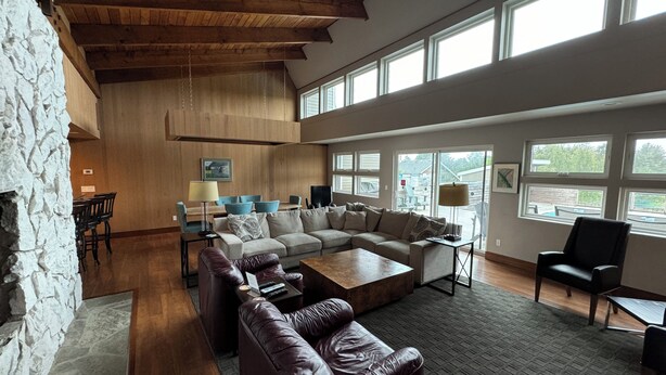 A spacious living room with a stone wall, wooden ceiling beams, a large sectional sofa, a leather armchair, and a coffee table. - Private Executive Home with Pool, Pickleball Court, and Sauna. (Gearhart)