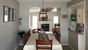 A dining area with a long table, chairs, a chandelier, and a fireplace.