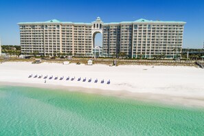 Un gran hotel con varios pisos y balcones, ubicado en una playa con aguas turquesas cristalinas.