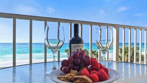 Une table avec une bouteille de vin Cooper & Thie Cellarmaster, deux verres à vin vides, une assiette de raisins et de noix, et une vue sur l’océan.