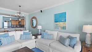 Un salon avec un canapé blanc, une table basse et un tableau représentant une scène de plage.