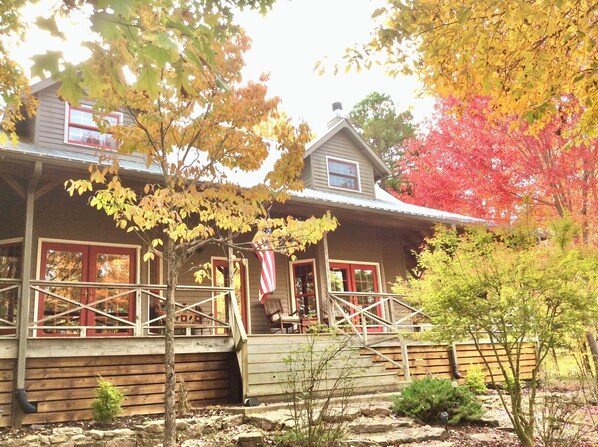 A wooden house with a porch, red-framed windows, and a flag.