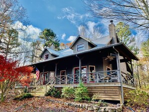 A two-story wooden cabin with a porch, a chimney, and a flag.