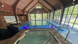 An indoor swimming pool with wooden architecture, a hot tub, and large windows.