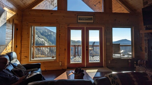 A cozy cabin interior with a high ceiling, wooden walls, and large windows offering mountain views.