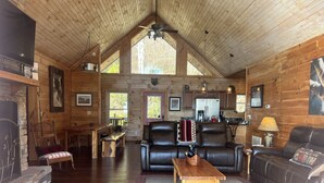 Interior acogedor de una cabaña con techo de madera, chimenea, comedor y sala de estar con mobiliario de cuero.